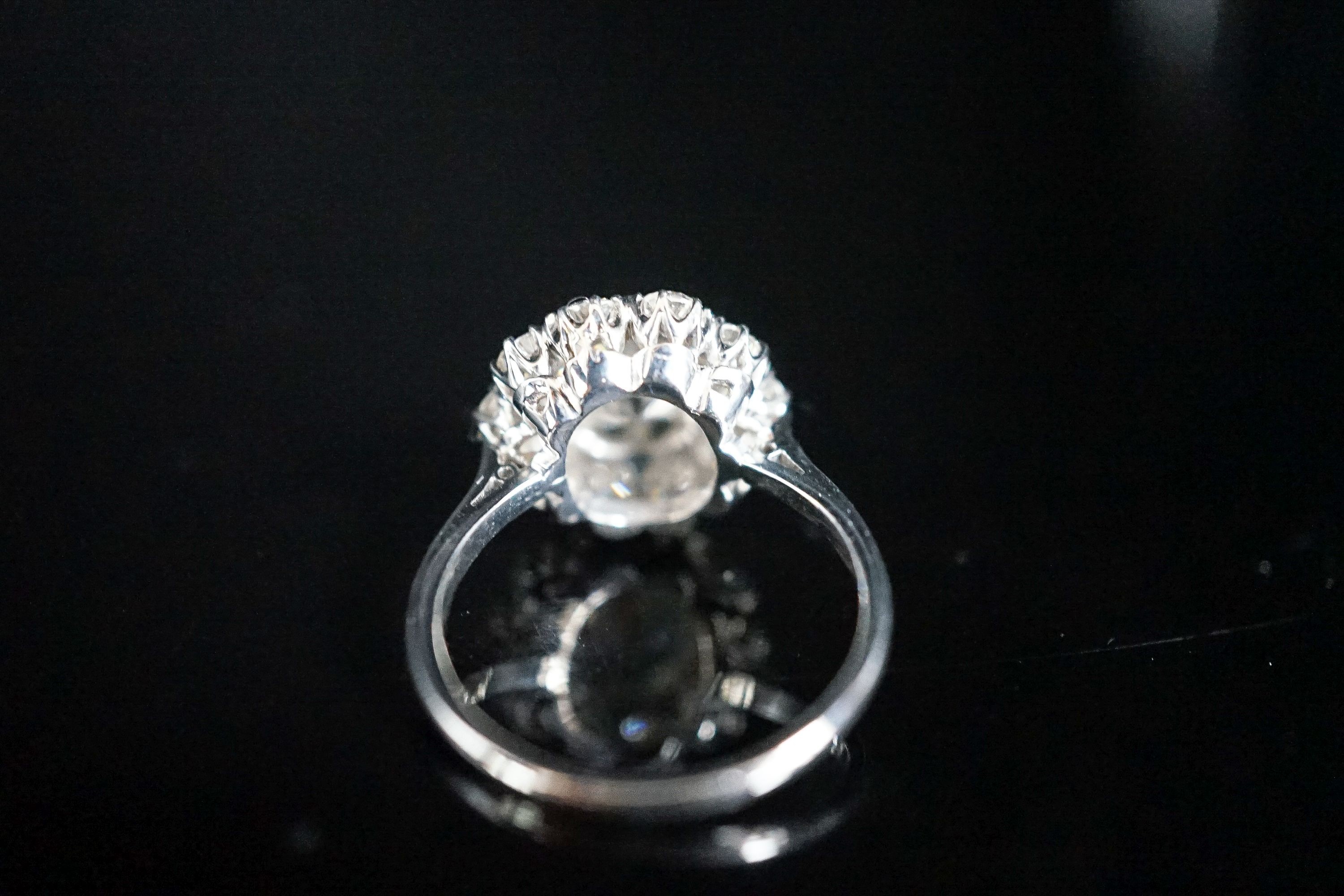 A white metal and eleven stone diamond set flower head cluster ring, the central stone weighing approximately 1.60ct, size N, gross 5 grams